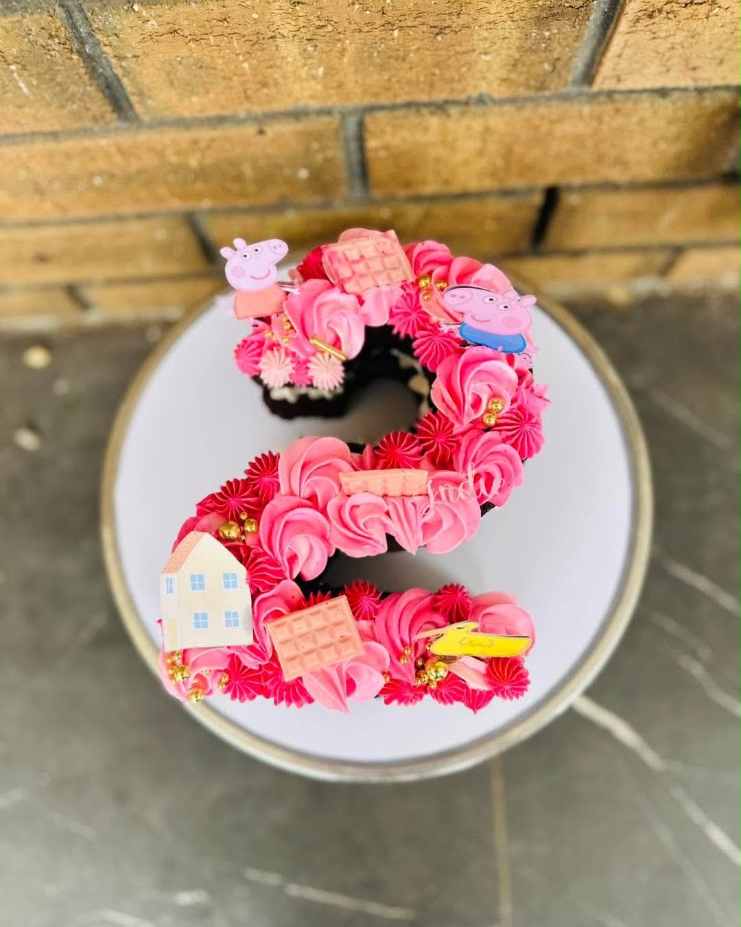 Pink number 2 shaped cake covered in hot pink and deep pink buttercream rosettes with Peppa Pig and George Pig toppers, waffle biscuits, a yellow car and a house for Indie